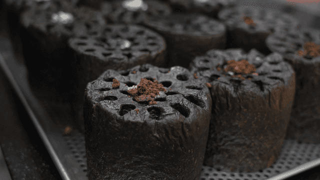 Baker pouring flour onto charcoal-shaped bun