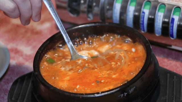 Soft bean curd jjigae in an hot pot stirred with a spoon