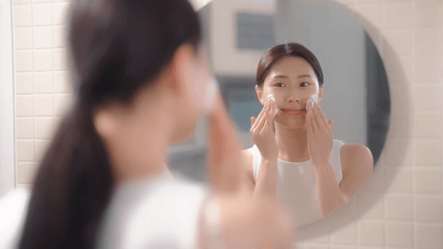 Woman applying facial cleanser in front of a mirror