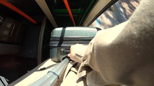 View of person boarding and sitting inside a bus with a suitcase
