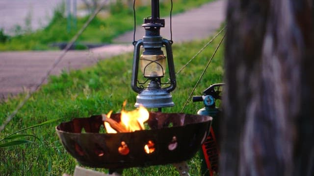 Man setting up a lantern near a campfire stove outdoors