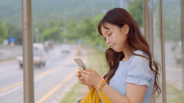 버스 정류장에서 휴대폰을 보는 여성의 옆모습