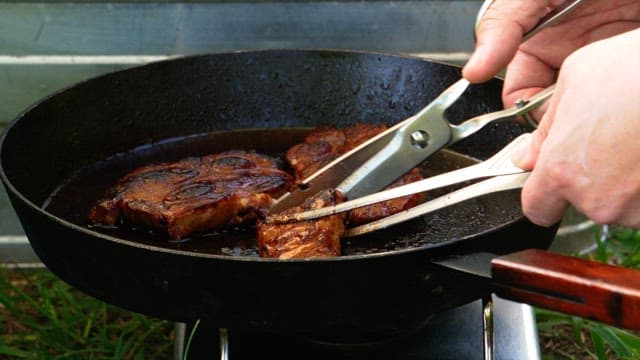 Grilling steaks on a hot frying pan, cutting with scissors