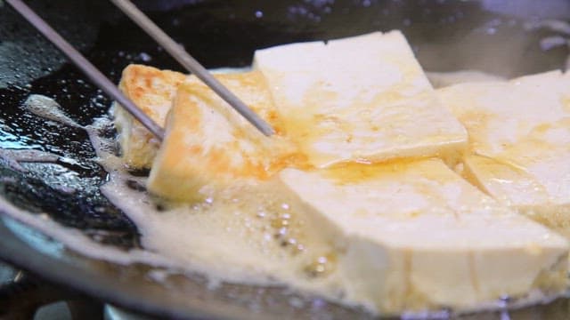 노릇하게 구워진 두부를 접시에 담는 장면