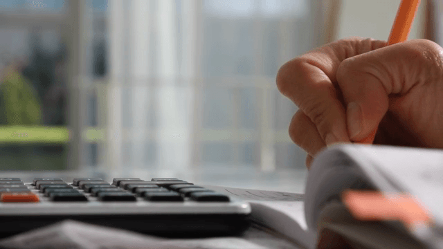 Hand writing in a notebook with a calculator