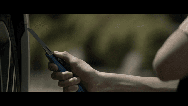 Student holding utility knife beside car tire