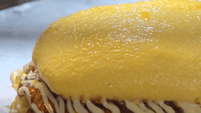 Egg omelet atop okonomiyaki with sauce