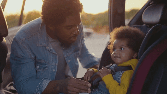 흑인 아빠가 아이를 카시트에 앉히는 모습