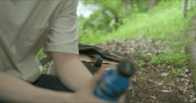 배낭 옆 야외에 앉아 음료수를 든 사람