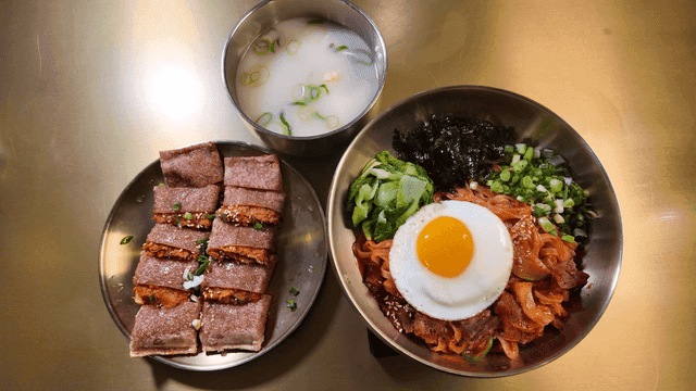 Bibim Kalguksu topped with egg yolk, buckwheat pancakes, beef bone broth