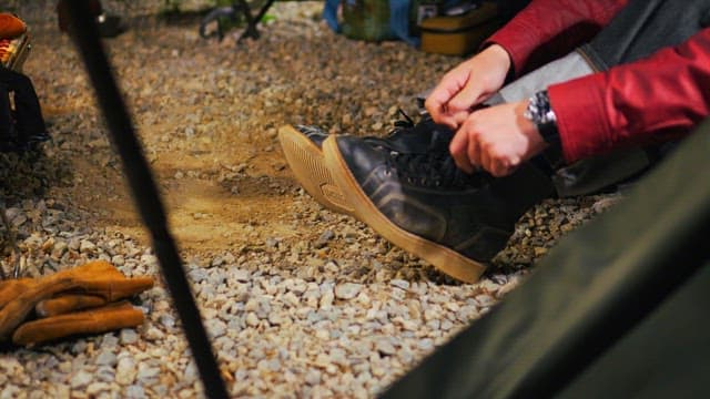 Camper tying shoes on a gravel campsite in early morning