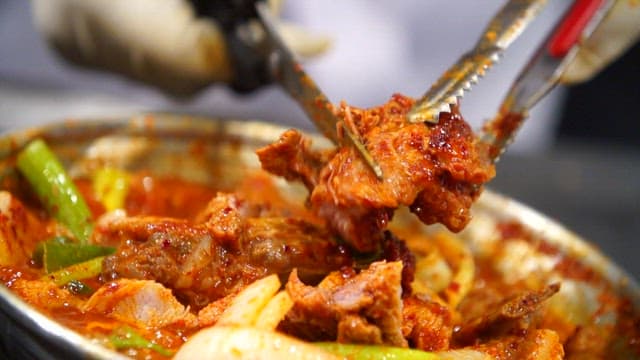 Cutting the meat of the spicy braised ribs boiling on the gas stove