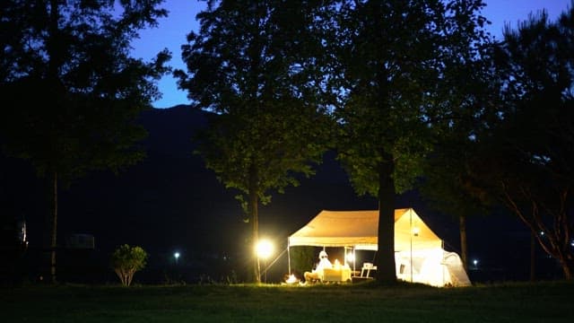 Person camping in the evening under illuminated tent