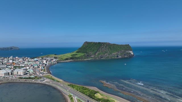 Seongsan Ilchulbong with Lush Greenery and Serene Coastal Village on a Sunny Day