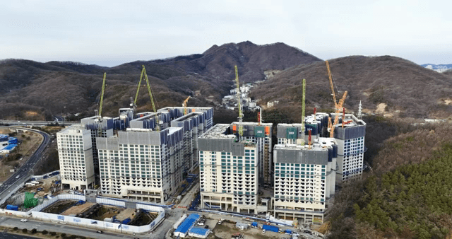 산 앞에 크레인과 건물이 있는 공사 현장