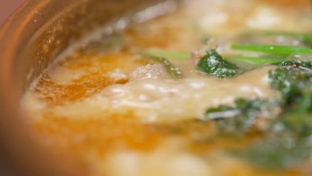 Steaming soup dish adorned with fresh water parsley and red chili