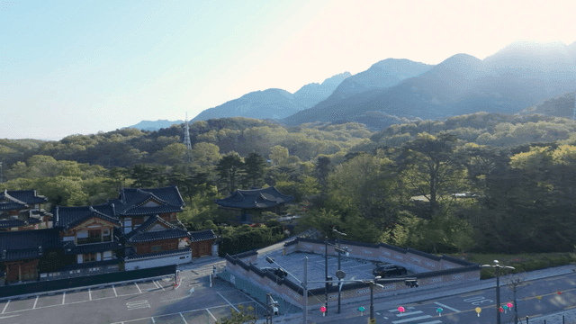 밝은 햇살이 비치는 전통 한옥 마을과 높은 산
