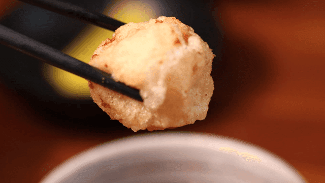 Chopsticks holding round piece of sweet and sour pork dipped in sauce