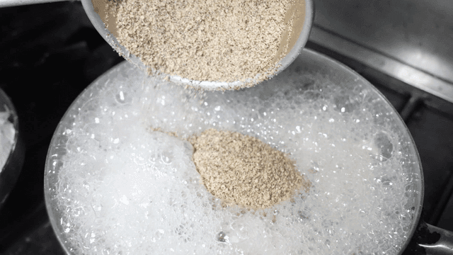 Ladle pouring ground perilla seed powder into boiling pot