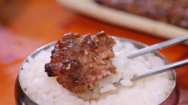 Grilled tteokgalbi on rice with chopsticks