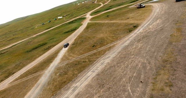 넓은 들판의 비포장 도로를 달리는 차