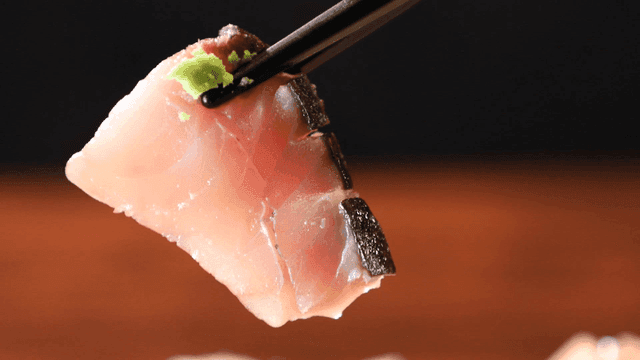 Piece of sashimi topped with wasabi, held with chopsticks