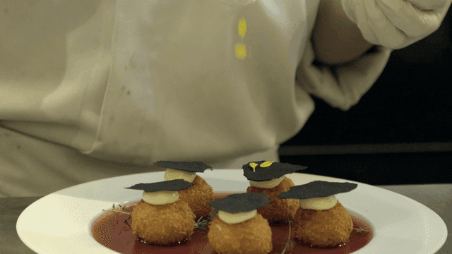Chef delicately sprinkles flowers on dish.