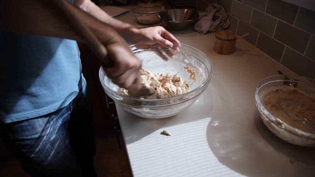 Man mixing dough in a glass bowl on a kitchen counter