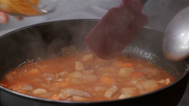 Cooking curry in a kitchen, spices being added and mixed in it