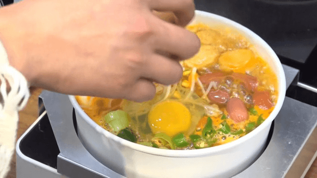 끓고 있는 각종 토핑이 있는 라면에 추가하는 계란