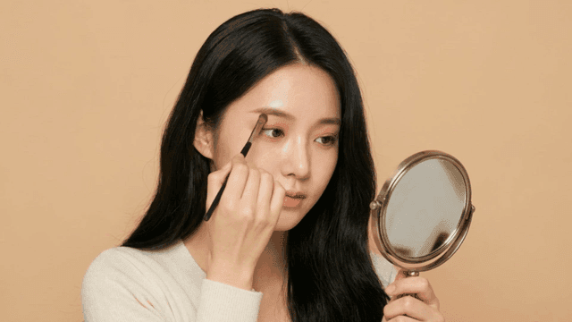 Woman applying eyeshadow with brush while looking in mirror