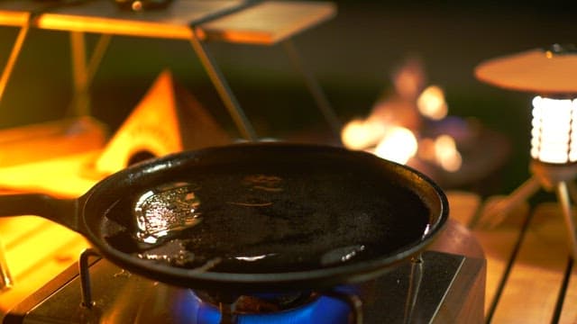 Skewered meat cooking on a pan over a gas burner at night