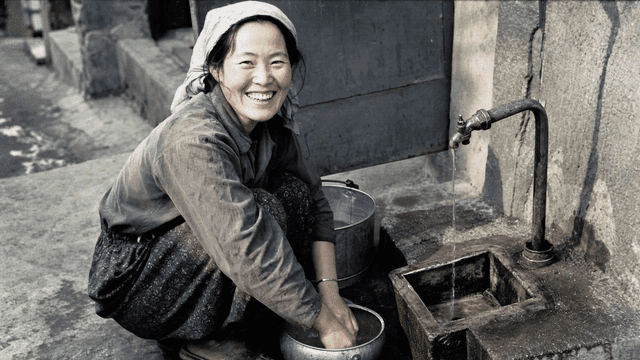 Woman smiling while washing dishes outdoors in 1970s