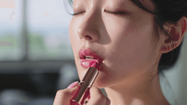 Young woman applying pink lipstick to her lips