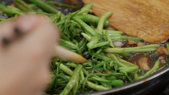 Stir-fried water parsley cooking in a frying pan with chopsticks