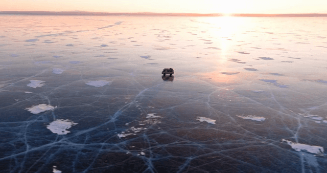 Vehicle on a vast frozen lake at sunset