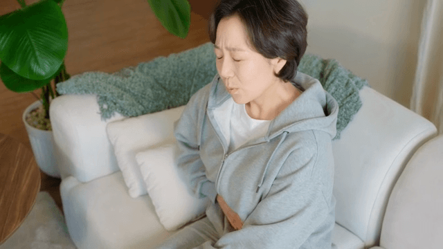소파에 앉아 배를 잡고 있는 여성
