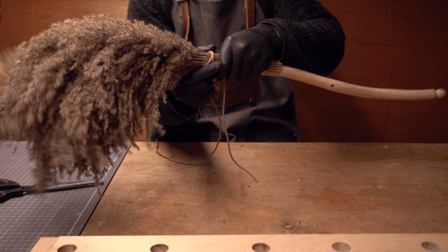 Craftsman tying reeds to a wooden handle