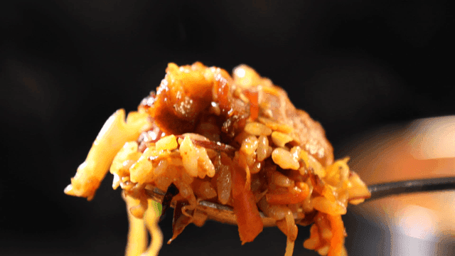 Spoon scooping up spicy oven-baked pork trotters mixed with vegetables
