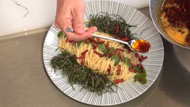 Adding seasoning to a plate of pasta with seaweed stems