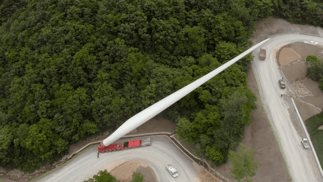 울창한 숲 속 구불구불한 도로에서 풍력 터빈 자재를 운반하는 모습