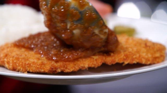 Sauce being poured over a crispy pork cutlet