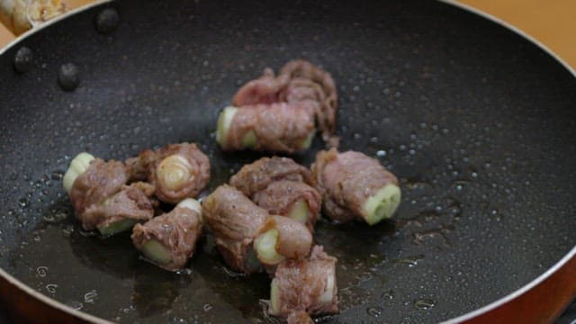 Green onion beef rolls cooking in a pan