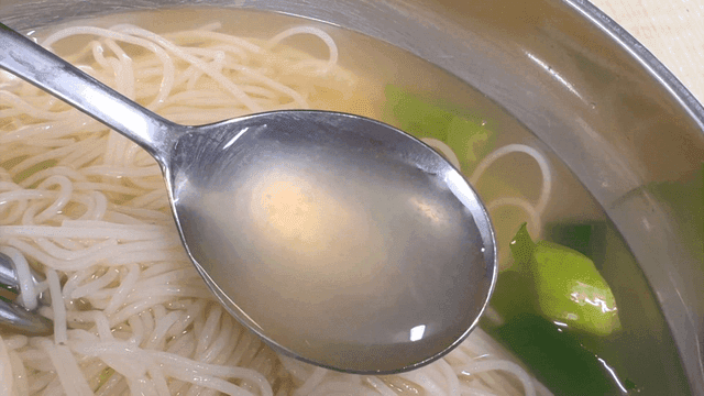 Lifting clear broth of vegetable banquet noodles by spoon
