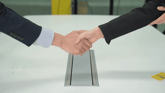 Two people shaking hands at a conference table
