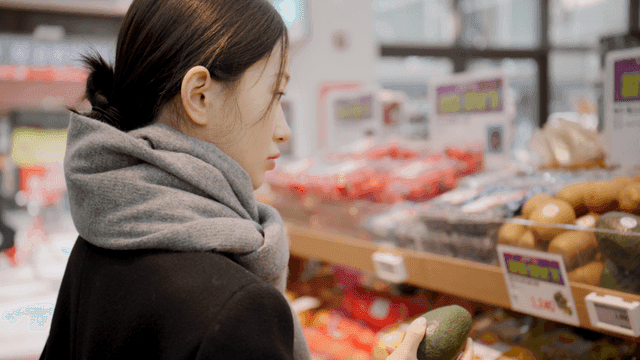 Young woman choosing avocado at grocery store