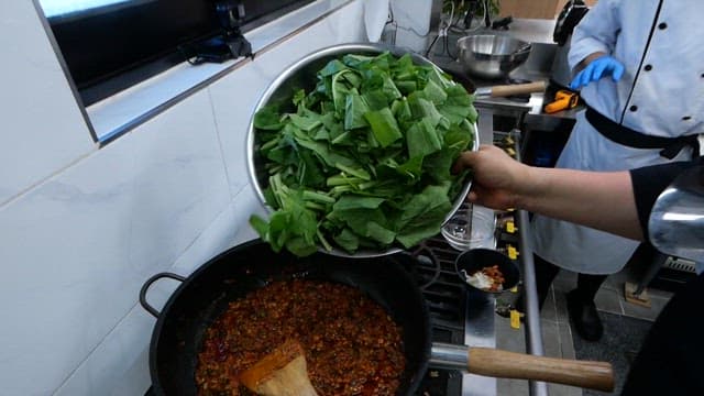 끓는 팬에 신선한 열무잎을 추가하는 요리사