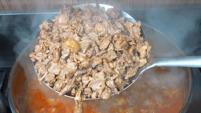 Ladle scooping beef soup from boiling pot