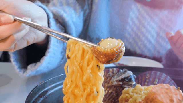Red scallop ramen picked up with chopsticks