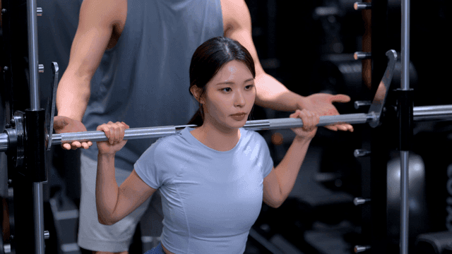 트레이너의 도움을 받아 스쿼트를 하는 젊은 여성